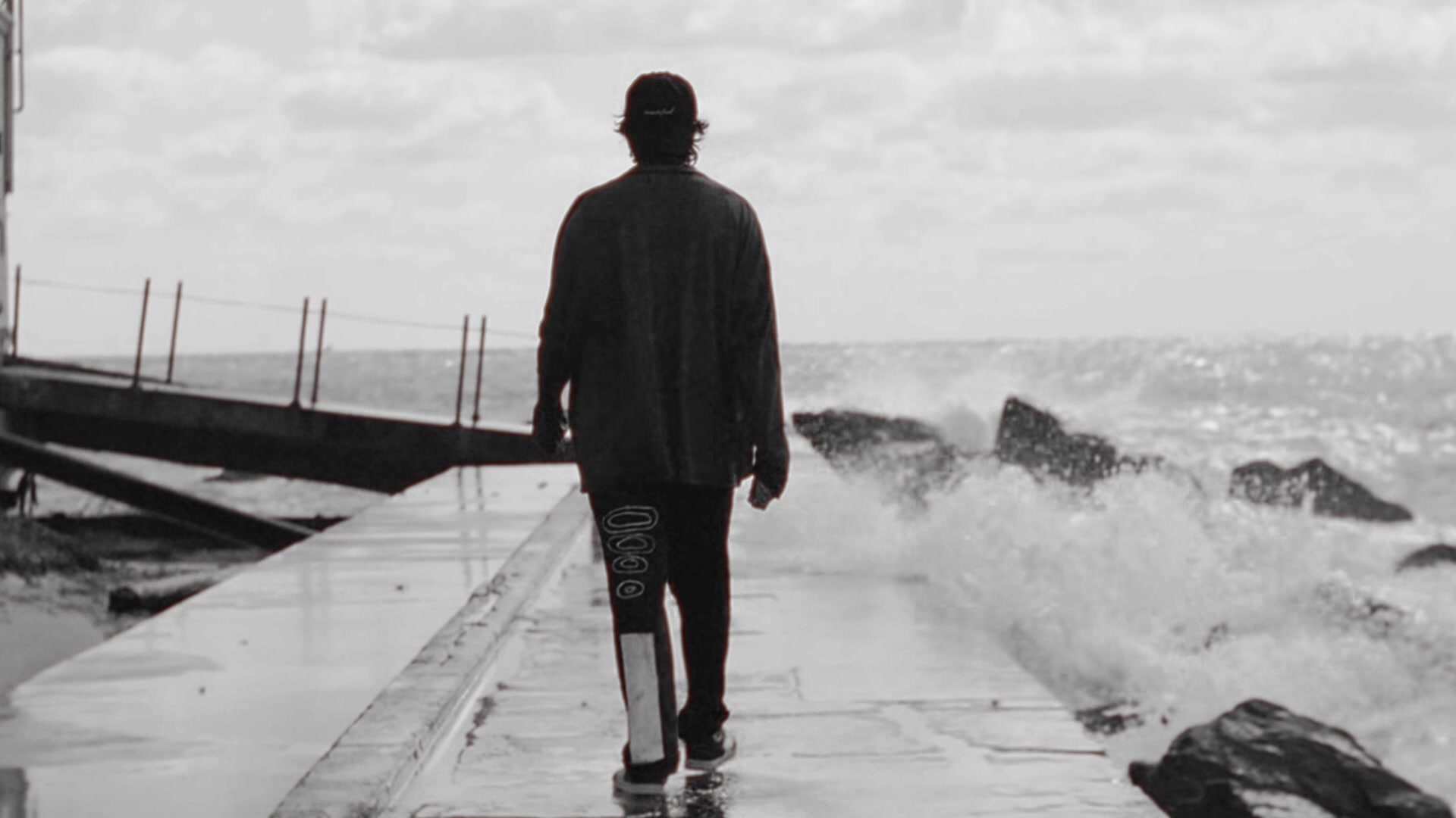 BRB walking the seawall as a wave breaks against the rocks